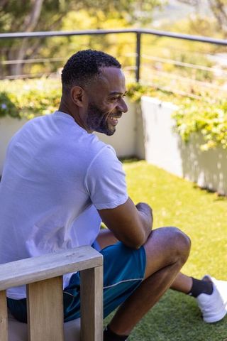 African american man sitting and smiling on sunlit balcony turf with casual athletic wear