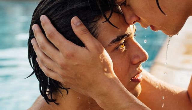 Cradling forehead kiss while partner leans over sunlit pool edge, intimate closeup