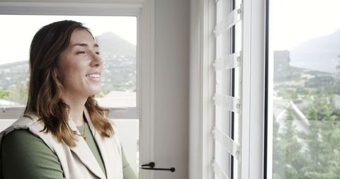 Woman Gazing Through Large Window with Mountain View, Smiling, Relaxed Lifestyle