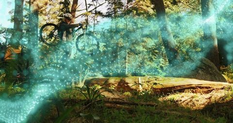 Mountain cyclist lifting bike over log on sunlit forest trail with turquoise light streaks