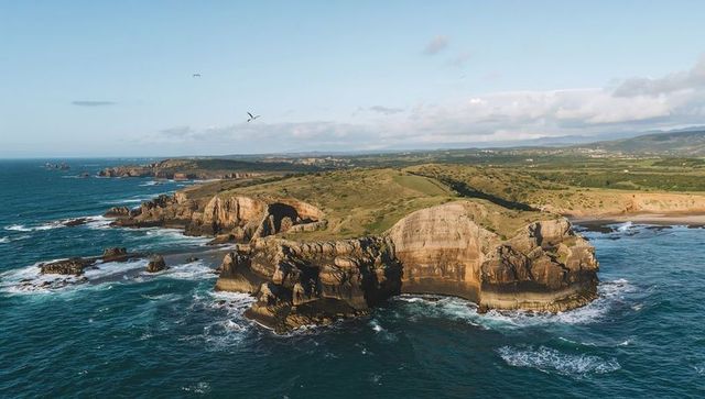 Dramatic layered headland with sea stacks and rolling grass plateau, aerial coastal view