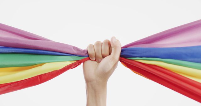Hand grasping brightly colored rainbow flag symbolizes LGBTQ pride, rights, and inclusivity. Useful for campaigns promoting human rights, awareness events, educational materials, and advocacy efforts.