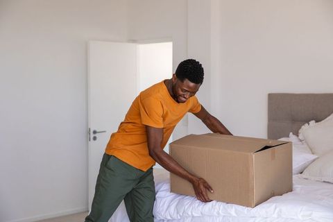 Man Handling Cardboard Box in Bright Minimalistic Bedroom