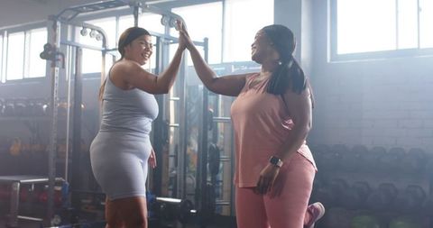 Diverse mid-adult women high-fiving and balancing during supportive gym workout