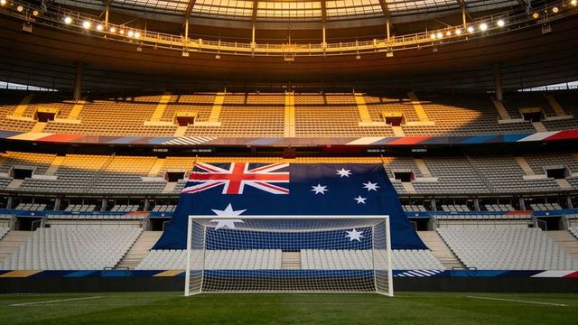Giant australian flag draping stadium stands behind soccer goal at empty roofed arena