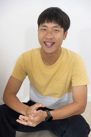 Smiling asian male wearing braces and smartwatch in yellow tee — casual lifestyle portrait