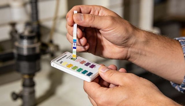 Hands comparing ph test strip to color chart, conducting precise water testing in lab