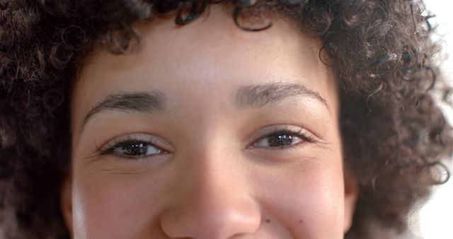 This image showcases a close-up of a young woman with curly hair and a warm smile. Her eyes appear bright and cheerful, expressing positivity and happiness. Ideal for use in beauty, wellness, and lifestyle advertisements, or any content promoting natural beauty and positive emotions. Great for blog posts, social media content, and marketing materials focused on skincare and self-care.