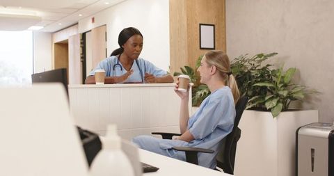 Healthcare team taking coffee break, female nurses chatting at clinic reception desk, smiling