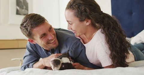 Couple Smiling While Playing with Dog on Bed at Home