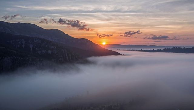 Sun rising over mist-filled alpine valley, silhouetted ridges, golden dawn panorama