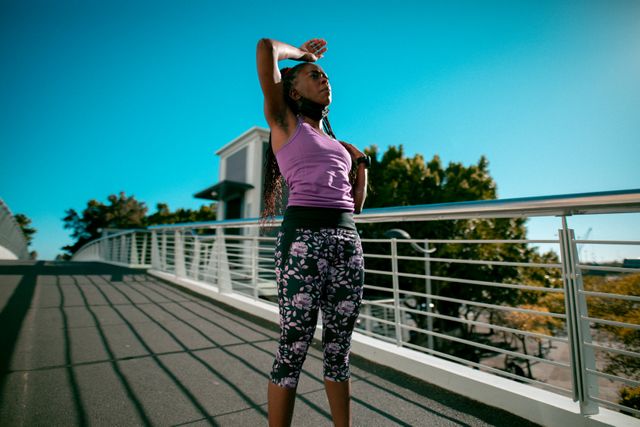 This image captures an African American woman engaging in outdoor exercise during sunset in an urban setting. Ideal for promoting healthy lifestyles, fitness programs, sportswear brands, and motivational content related to physical activity and wellness.