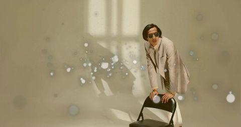 Stylish man in beige suit with sunglasses leaning on chair