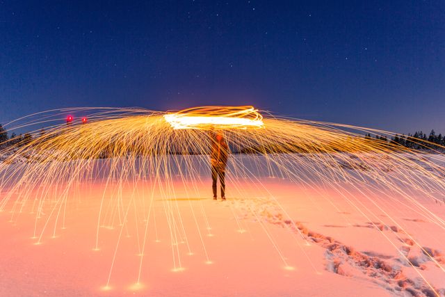 This dynamic image captures a person creating vibrant sparkler art below a clear night sky in a snowy landscape, illustrating creativity and seasonal enjoyment. Perfect for illustrating winter recreational activities, holiday creativity, light painting techniques, or scenic winter backdrops.