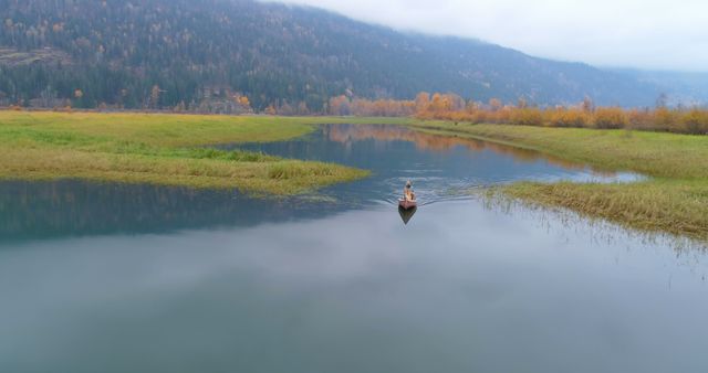 Person canoeing on a tranquil lake surrounded by colorful autumn forest and mountainous landscape. Perfect for portraying peacefulness, adventure, outdoor activity, travel, nature scenery, tourism, and solitude.