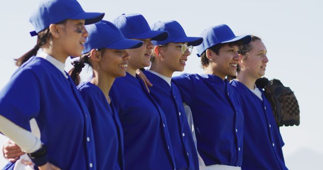 Happy diverse team of female baseball players standing in line with arms around each other singing. female baseball team, sports training and game tactics.