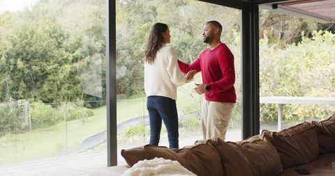 Couple standing by floor-to-ceiling glass doors overlooking lush wooded backyard