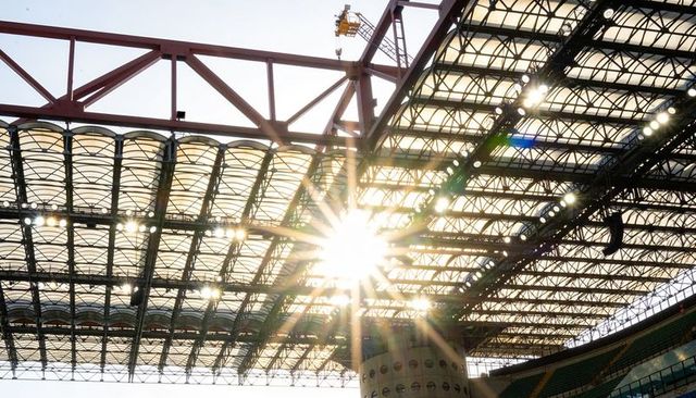 Sunburst piercing stadium roof structure revealing steel trusses, floodlights, glass canopy