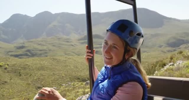 Woman exploring picturesque mountain scenery wearing zip lining gear. Ideal for content about adventure tourism, outdoor activities, and travel inspiration. Perfect for illustrating the beauty of nature and the thrill of exploration in remote areas.