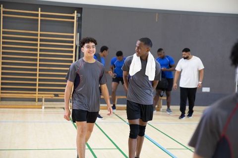 Teen athletes walking and talking in school gym after basketball practice with coach