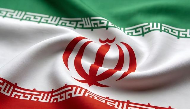 Waving iran flag closeup showing red emblem and kufic script border on tricolor fabric