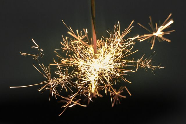 Close-up image of a sparker with intense sparks illuminating the surrounding area against a dark background. Perfect for festive celebrations, New Year's Eve promotions, holiday party advertisements, and event invitations.