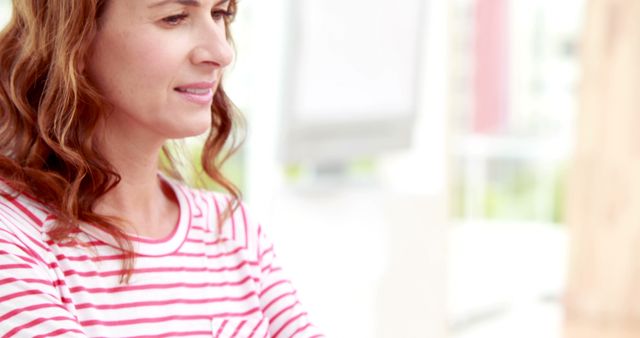 Woman in striped shirt staring at screen or document, appearing thoughtful and focused. Ideal for business, office work, casual work environment, project management, remote work, or women's workplace themes.