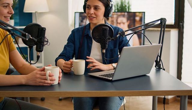 Two women co-hosts recording conversational podcast in home studio with headphones, microphones