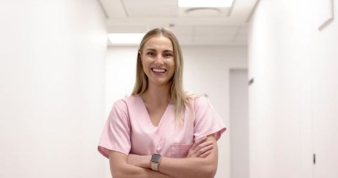 Smiling healthcare professional standing in bright clinic corridor wearing pink scrubs