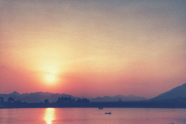Serene Sunset Over Calming Lake with Silhouetted Boat and Mountains - Download Free Stock Photos Pikwizard.com