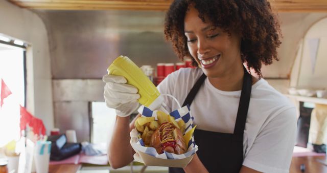 African american woman wearing apron putting mustard over the hot dog in food truck. food truck and street food concept