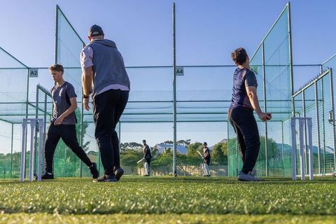 Cricket coaching session with young players practicing bowling and batting in outdoor nets