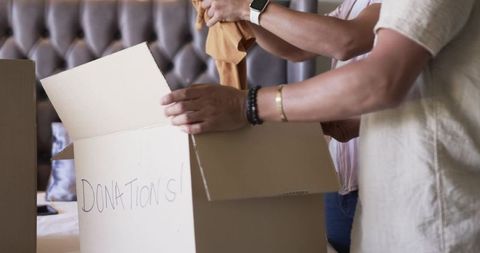 Volunteers packing clothing donations into cardboard box on bed for charity drive