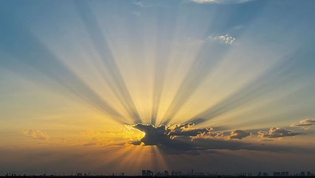 Golden sunburst crepuscular rays radiating from cloud over city skyline at sunrise