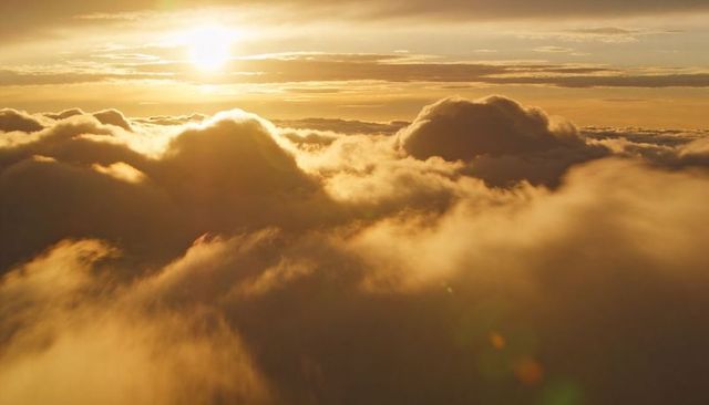 Golden sunrise casting warm light over voluminous cumulus cloudscape at high altitude