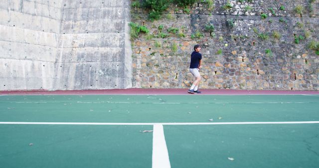 Man practicing tennis by hitting ball against wall on an outdoor court. Ideal for content related to sports, fitness, and outdoor activities.