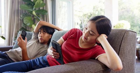 Couple relaxing on sofa using smartphones in cozy living room