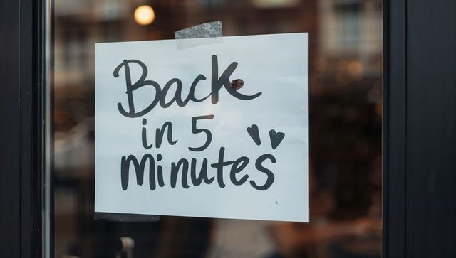Handwritten back in 5 minutes sign taped on cafe door with hearts and warm reflections
