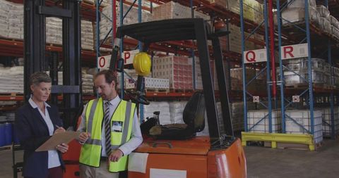 Warehouse managers reviewing inventory near forklift improving logistics efficiency