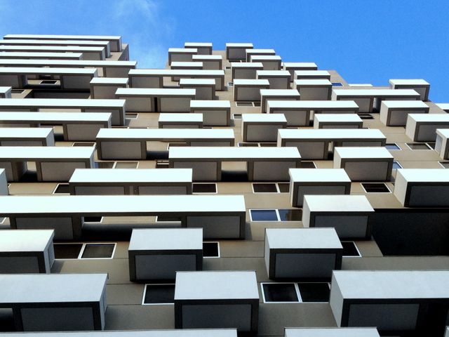 Image depicts a modern apartment building with a unique geometric facade against a clear blue sky. It showcases innovative urban architecture and design, ideal for use in articles about contemporary urban living, architectural magazines, real estate promotions, construction advertisements, or interior design websites.