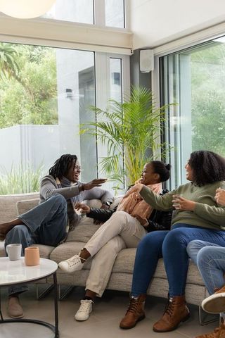 African american friends laughing and chatting on cozy sectional sofa in sunlit modern living room