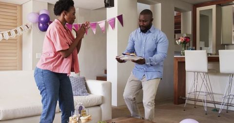African American couple celebrating birthday at home sharing cupcakes and joyful surprise