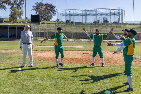 Baseball Players in Green and Yellow Stretching with Coach on Infield during Warmup Drills