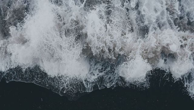 Crashing waves curling along dark shoreline with frothy surf aerial view