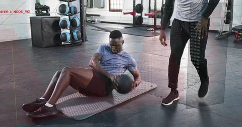 Man performing russian twist with medicine ball while trainer coaching indoor core session