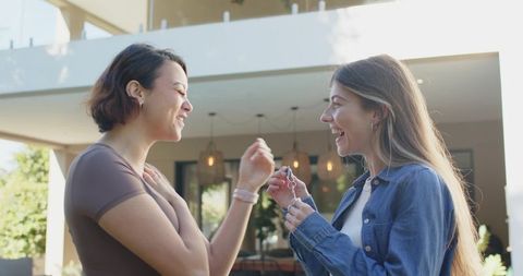 Friends celebrating new homeownership: two women handing over keys on modern sunlit porch
