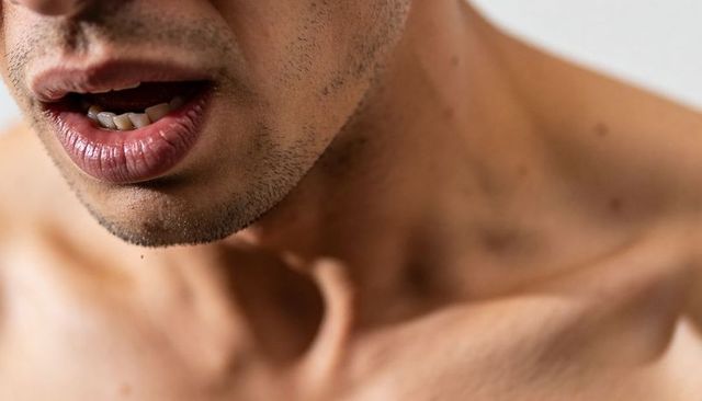 Shirtless male showing stubbled jawline and lips with visible teeth and collarbone close-up
