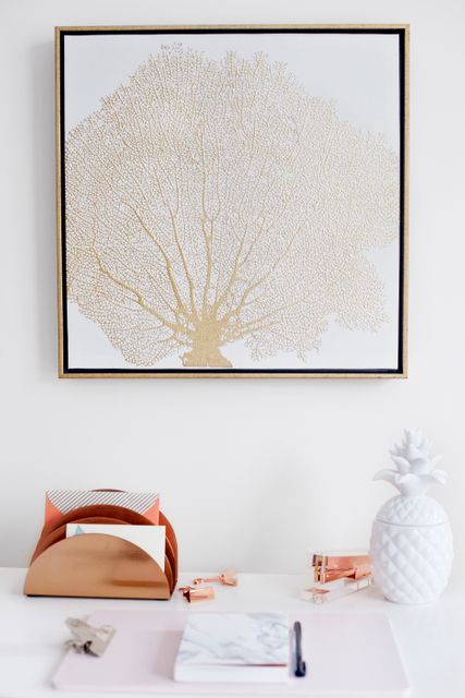 Desktop featuring peach folder organizer, white pineapple ornament, gold and white coral artwork. Perfect for illustrating stylish desk arrangements, work-from-home setups, modern office decor, organization, and contemporary working environments.