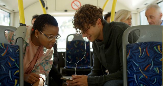 Diverse couple shares music on a bus ride. They enjoy a moment of connection while commuting, surrounded by other passengers.