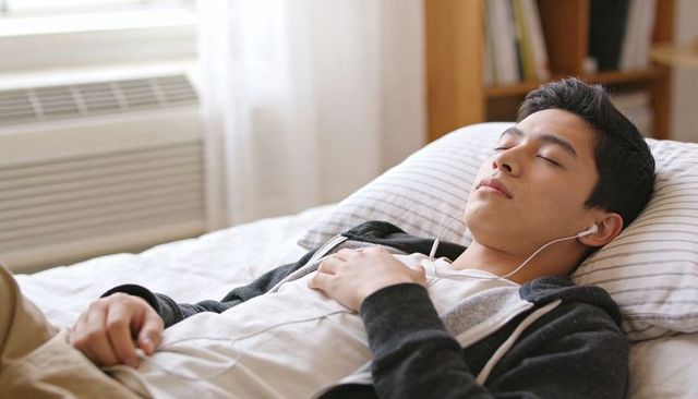 Teen listening to music on bed with earbuds resting with eyes closed in hoodie